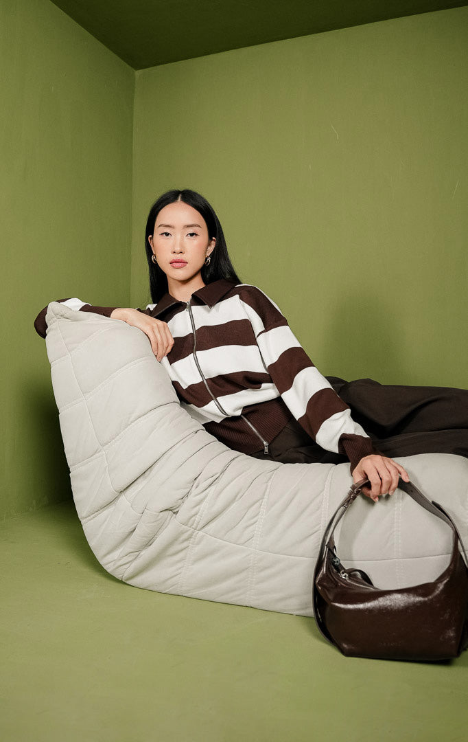 Sweater rajut wanita Reese Sweater lengan panjang dengan motif garis horizontal lebar berwarna cokelat dan putih, dilengkapi bukaan resleting depan penuh (full zip) dan detail kerah beraksen kulit sintetis warna cokelat.