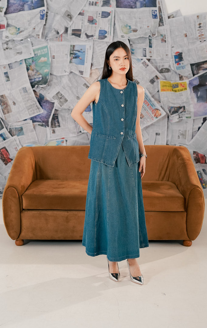 Model mengenakan Renaka Top Denim, atasan wanita bahan denim biru yang kokoh (sturdy), potongan tanpa lengan (sleeveless) dengan kancing depan yang bisa dijadikan vest.