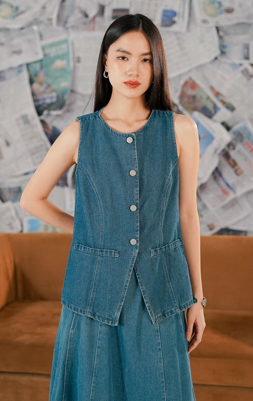 Model mengenakan Renaka Top Denim, atasan wanita bahan denim biru yang kokoh (sturdy), potongan tanpa lengan (sleeveless) dengan kancing depan yang bisa dijadikan vest.