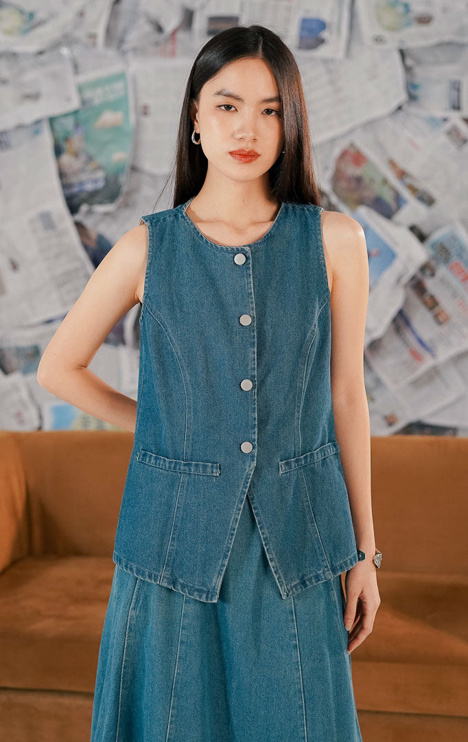 Model mengenakan Renaka Top Denim, atasan wanita bahan denim biru yang kokoh (sturdy), potongan tanpa lengan (sleeveless) dengan kancing depan yang bisa dijadikan vest.