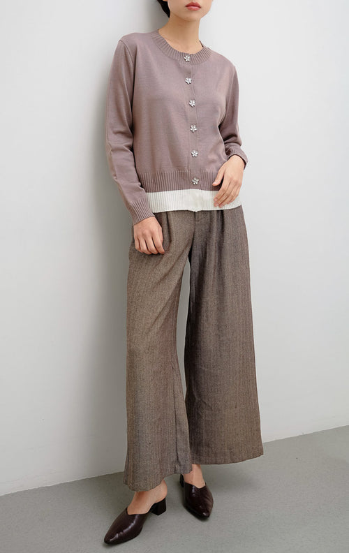 Cardigan rajut wanita warna cokelat (brown) Revie Cardigan dengan detail kancing bentuk bunga (floral button), aksen pinggiran warna ivory, dan siluet relaxed fit.