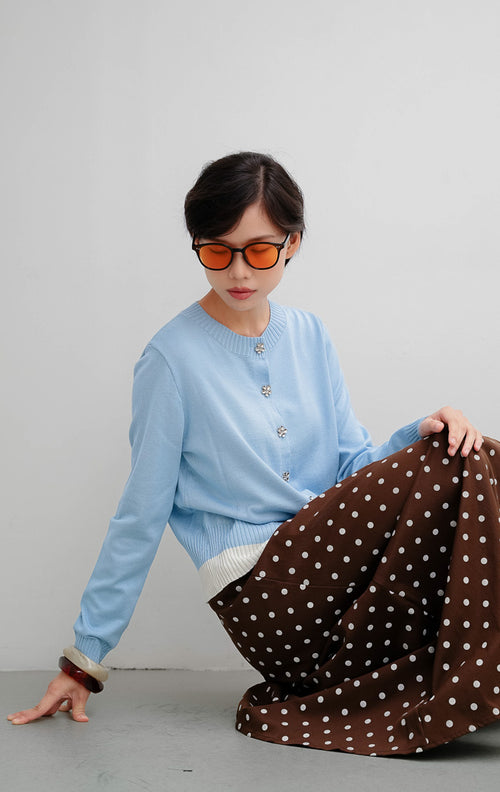 Cardigan rajut wanita warna biru muda (light blue) Revie Cardigan dengan detail kancing bentuk bunga (floral button), aksen pinggiran warna ivory, dan siluet relaxed fit.
