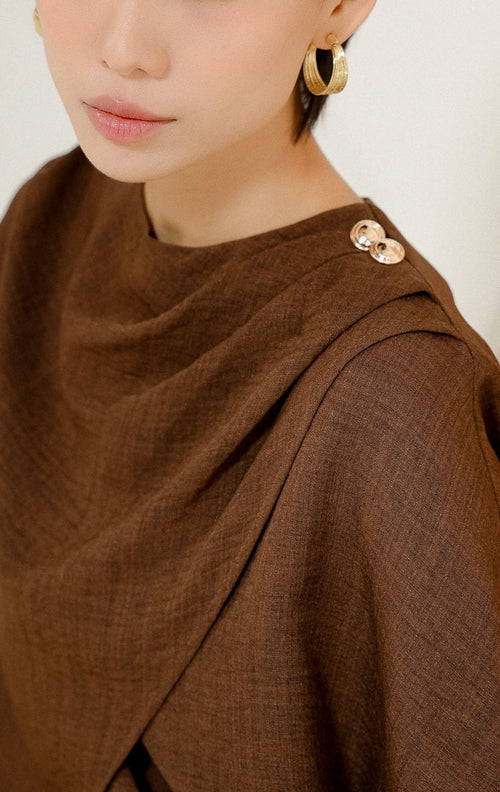 Close-up detail kerah dan bahu Rhayn Wrap Blouse Top Dark Brown, menampilkan tekstur kain cokelat tua dengan desain silang wrap dan dua kancing emas dekoratif. 