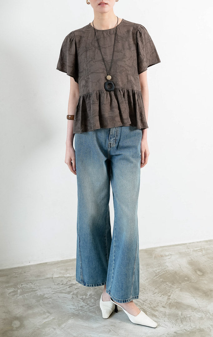 Atasan wanita lengan pendek warna cokelat tua (dark brown) Rivena Top berbahan tekstur crinkle ringan (lightweight crinkle texture) dengan kerah bulat (round neckline) dan detail bagian bawah bertingkat kerut (softly gathered tiered hem). 

