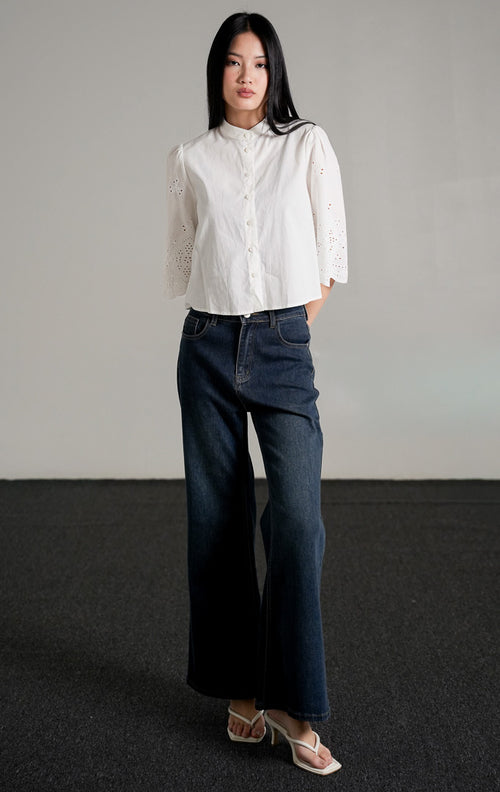 Rochelle Top White, kemeja katun warna putih dengan detail bordir eyelet pada lengan pendek yang melebar, dipadukan dengan celana jeans biru gelap.