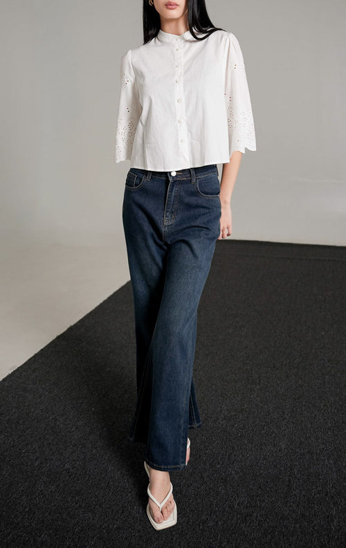 Rochelle Top White, kemeja katun warna putih dengan detail bordir eyelet pada lengan pendek yang melebar, dipadukan dengan celana jeans biru gelap.