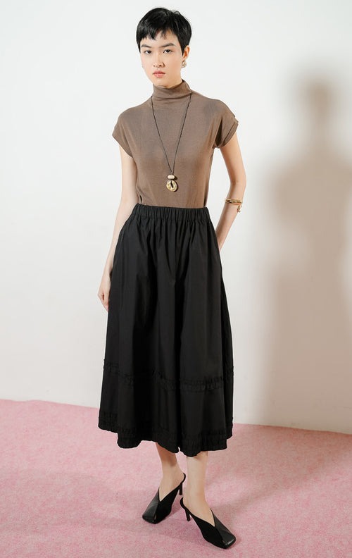 Model wanita mengenakan Arabella Skirt warna black, rok midi panjang wanita berwarna hitam dengan pinggang karet dan detail aksen kerut ruffle horizontal.