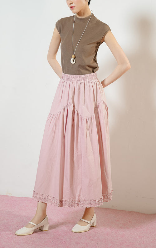 Model wanita mengenakan Lacey Tiered Ruffle Hem Skirt warna dusty pink, rok panjang katun wanita berwarna merah muda dengan pinggang karet dan detail kelim kerut rumbai yang feminin. 