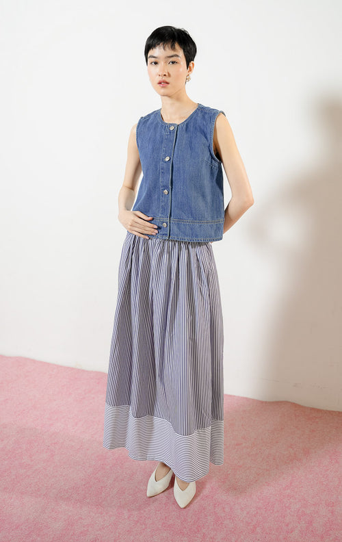 Model wanita mengenakan Klyne Round-Neck Button Vest Denim, atasan rompi vest denim wanita berwarna biru dengan potongan kerah bulat dan kancing depan logam. 