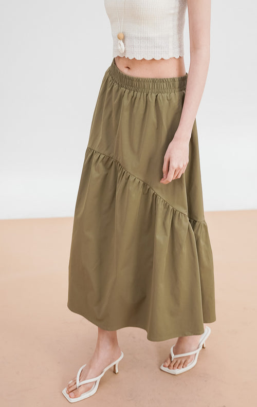  Model mengenakan Rosalia Skirt warna dark green, rok panjang bertingkat (tiered) dengan detail pinggang elastis, dipadukan dengan crop top broken white.