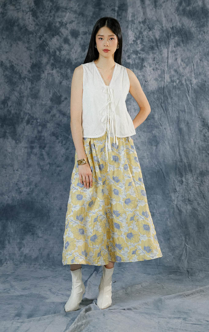Atasan vest wanita Rosalind warna putih bersih tanpa lengan dengan detail katun embroidery, kerah v-neck berenda (lace), dan aksen tali pita depan. 