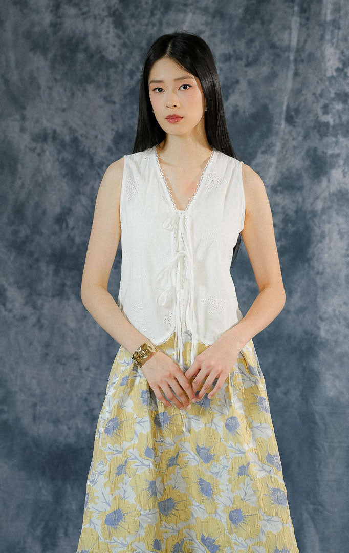 Atasan vest wanita Rosalind warna putih bersih tanpa lengan dengan detail katun embroidery, kerah v-neck berenda (lace), dan aksen tali pita depan. 