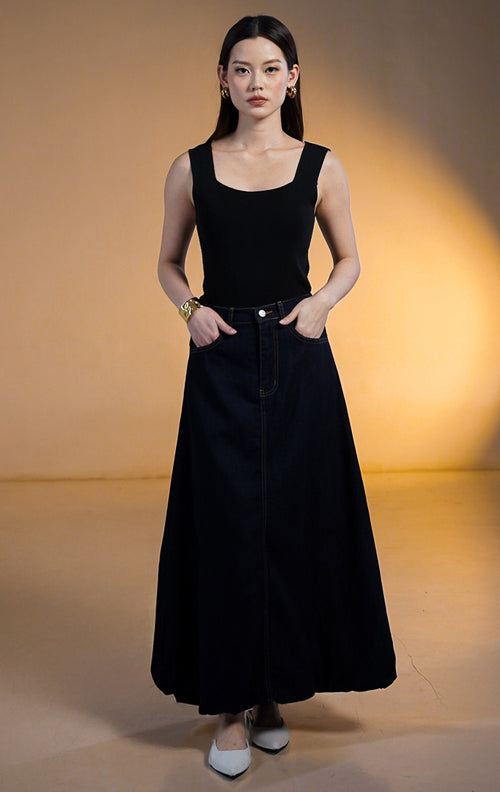 Model wanita memakai Rouje Skirt Dark Denim, rok panjang jeans biru tua dengan potongan balon bervolume dan saku samping, dipadukan dengan tank top hitam