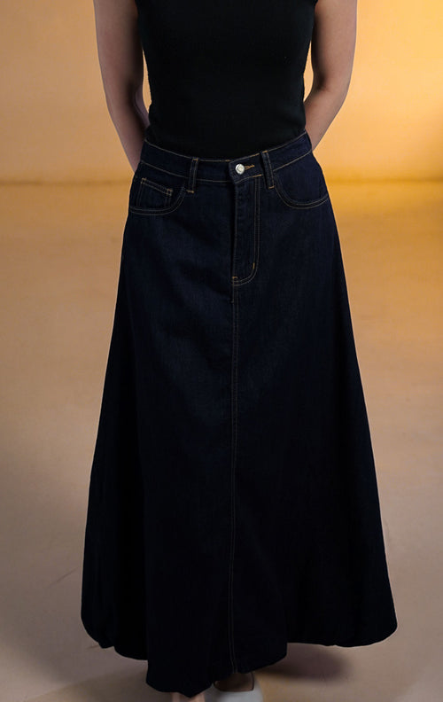 Model wanita memakai Rouje Skirt Dark Denim, rok panjang jeans biru tua dengan potongan balon bervolume dan saku samping, dipadukan dengan tank top hitam