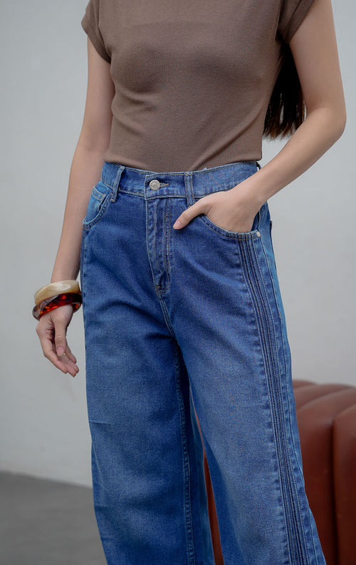 Celana jeans wanita model lurus (straight leg) warna biru medium (denim) Rovex Pants dengan aksen jahitan lipit samping (pintuck detailing), saku fungsional, dan pinggang karet belakang. 