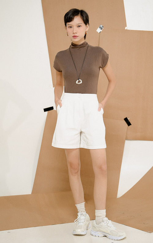 Model berdiri mengenakan Rowan Minimal Classic Short Pants White, produk celana pendek wanita warna putih dengan siluet high-waisted minimalis dan saku samping. 