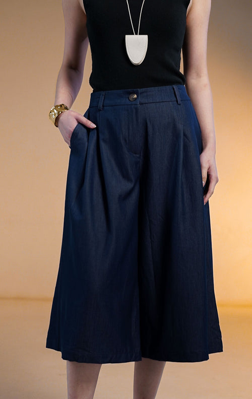 Model wanita memakai Ruben Pants Dark Denim, celana kulot bermuda lebar warna biru tua dengan saku samping, dipadukan dengan tank top hitam dan kalung putih