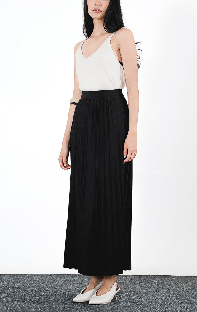 Ryka Skirt warna hitam, rok midi plisket (pleated) siluet A-line yang rapi dengan ban pinggang elastis, dipadukan dengan atasan tanpa lengan putih.