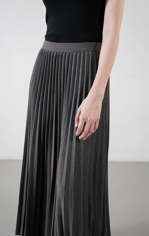 Ryka Skirt warna dark grey, rok midi plisket (pleated) siluet A-line yang rapi dengan ban pinggang elastis, dipadukan dengan sandal hitam.1