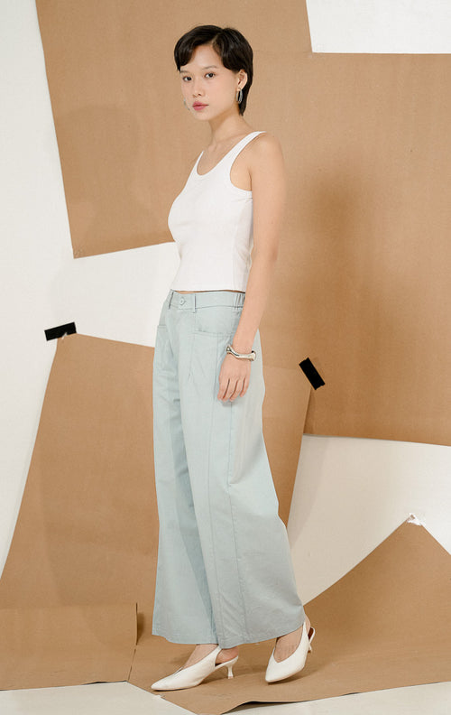 Model berdiri dengan tangan di saku mengenakan Sapphire Straight Leg Pants Light Blue, produk celana panjang wanita potongan lurus warna biru muda dengan detail kancing depan. 