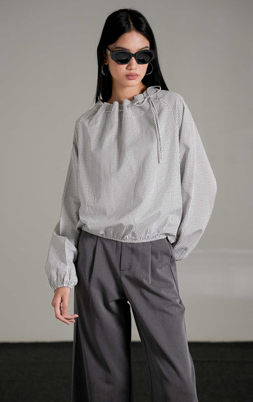 Seraph Top White, atasan katun putih motif kotak grid halus dengan leher serut (drawstring), dipadukan dengan celana kulot abu-abu dan kacamata hitam.