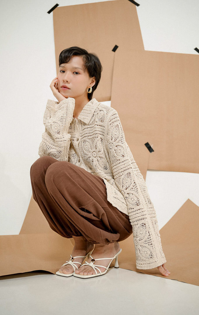 Model berpose jongkok mengenakan Sevyn Granny Square Crochet Cardigan Ivory, luaran cardigan rajut wanita lengan panjang warna krem dengan motif rajutan transparan. 