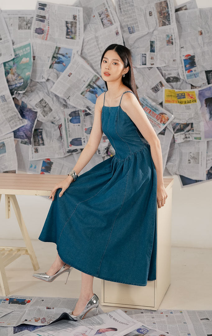 Model mengenakan Shanon Dress Denim, sebuah maxi dress wanita bahan denim biru yang kokoh, model tanpa lengan (sleeveless) dengan potongan panjang yang santai dan elegan.