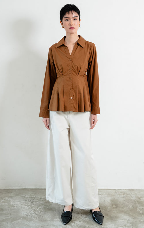 Kemeja wanita lengan panjang warna cokelat (brown) Shea Top dengan kerah kemeja (pointed collar), leher V (V-neckline), bukaan kancing depan, dan detail lipit di pinggang (pleated waist). 

