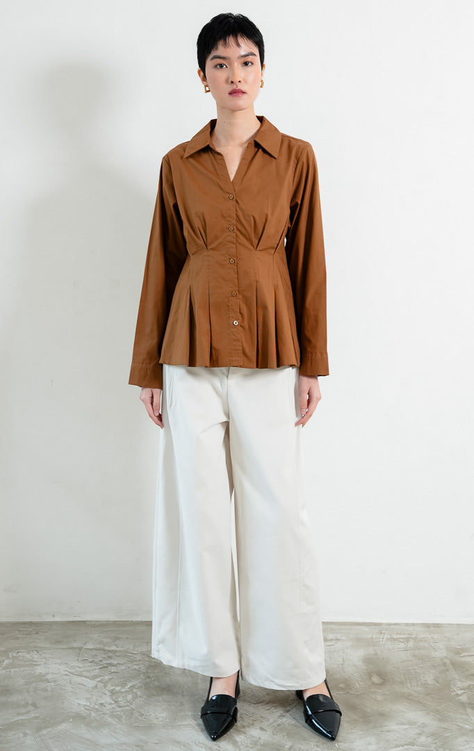 Kemeja wanita lengan panjang warna cokelat (brown) Shea Top dengan kerah kemeja (pointed collar), leher V (V-neckline), bukaan kancing depan, dan detail lipit di pinggang (pleated waist). 

