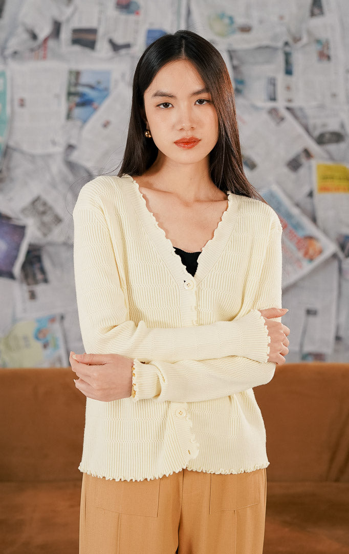 Model mengenakan Shera Cardigan Yellow, luaran rajut wanita warna kuning cerah dengan detail pinggiran scallop yang feminin, bahan melar (stretch), dan kancing depan.