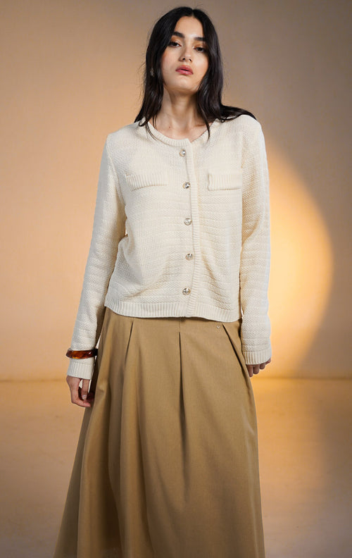 Model wanita memakai Shiloh Outer Ivory, cardigan rajut lengan panjang warna cream bertekstur dengan saku dekoratif dan kancing emas, dipadukan dengan rok panjang coklat