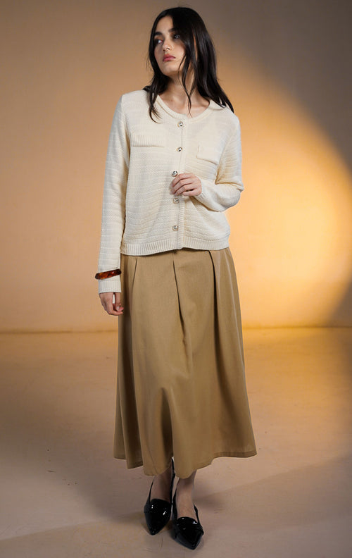Model wanita memakai Shiloh Outer Ivory, cardigan rajut lengan panjang warna cream bertekstur dengan saku dekoratif dan kancing emas, dipadukan dengan rok panjang coklat