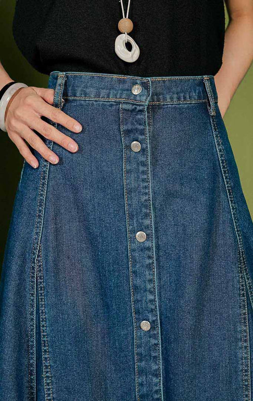 Rok panjang wanita Solde Skirt berbahan denim warna biru gelap (dark denim) dengan siluet A-line, dilengkapi detail jahitan panel vertikal yang rapi, tempat sabuk (belt loops), dan deretan kancing metal penuh di bagian tengah depan.