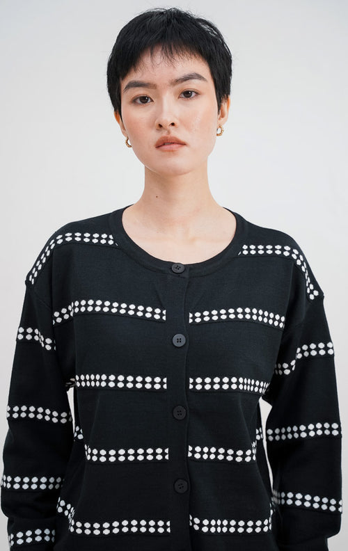 Model mengenakan Soleil Cardigan warna black, kardigan rajut lengan panjang dengan motif garis horizontal titik-titik putih dan kancing bulat hitam di bagian depan.