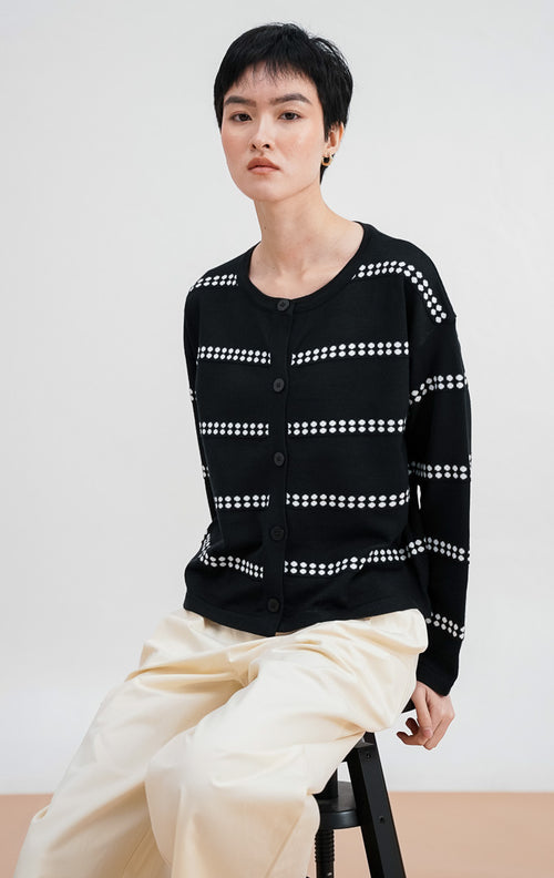  Model mengenakan Soleil Cardigan warna black, kardigan rajut lengan panjang dengan motif garis horizontal titik-titik putih dan kancing bulat hitam di bagian depan.