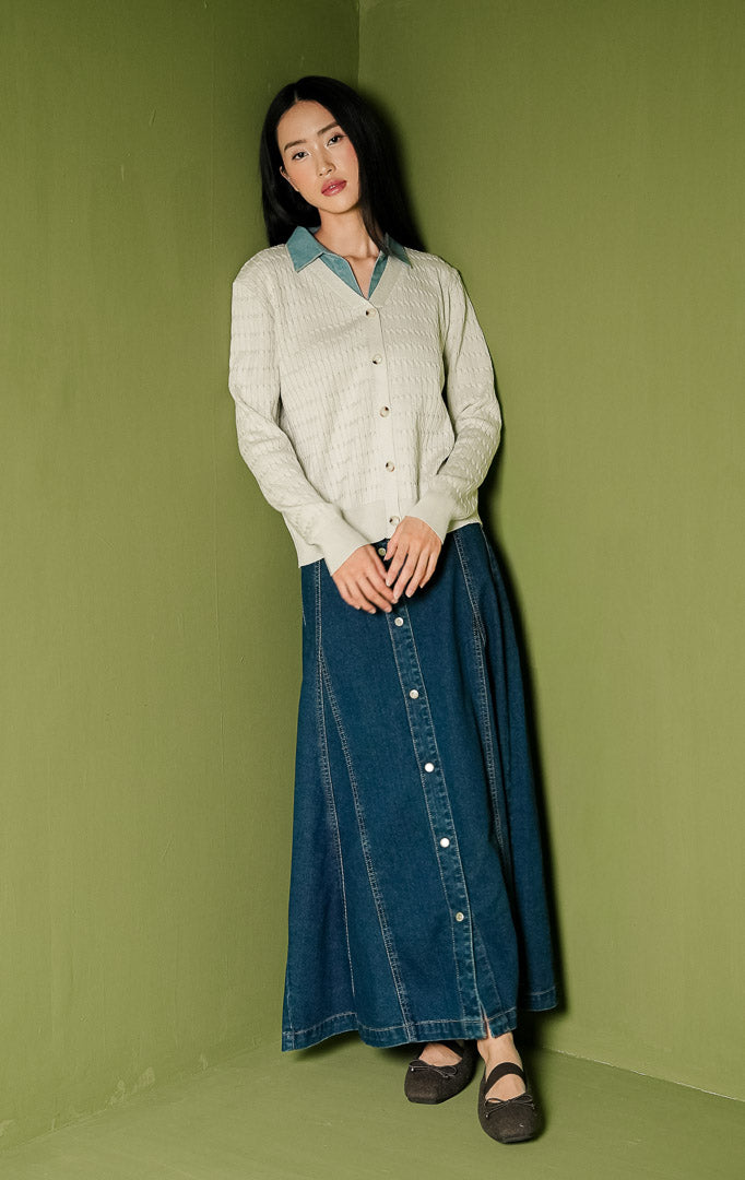 Kardigan rajut wanita Solene Outer lengan panjang warna ivory, memiliki tekstur rajut pola kepang vertikal, dilengkapi aksen lapisan kerah bahan denim biru kontras pada bagian leher V-neck, serta deretan kancing depan bernuansa cokelat.