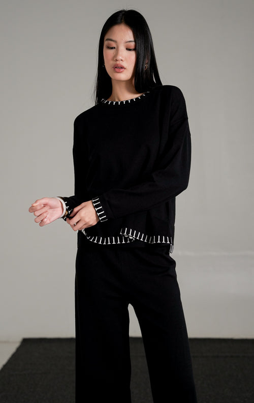 Soobin Knit Set warna hitam, yang terdiri dari atasan lengan panjang dan celana panjang rajut berpotongan longgar dengan detail jahitan pola putih di bagian ujung.