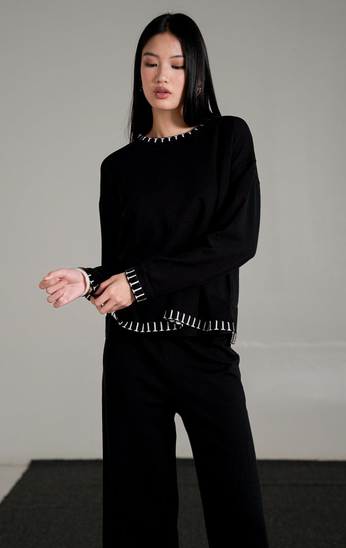 Soobin Knit Set warna hitam, yang terdiri dari atasan lengan panjang dan celana panjang rajut berpotongan longgar dengan detail jahitan pola putih di bagian ujung.