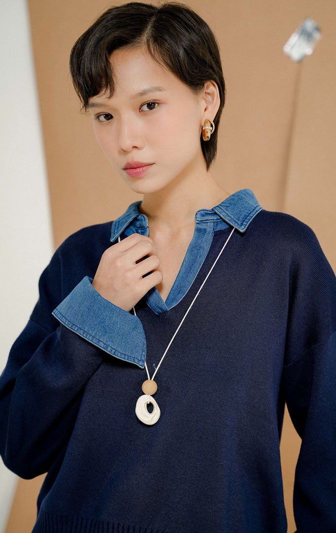 Model berdiri mengenakan Sophia Denim Collar Knit Sweater Navy, produk sweater rajut wanita lengan panjang warna biru dongker dengan variasi kerah kemeja dan manset lengan denim. 