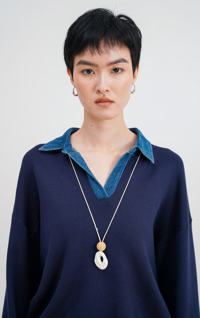 Close-up model mengenakan Sophia Sweater warna navy, menampilkan detail kerah denim biru yang kontras dengan bahan rajut halus dan kalung statement.