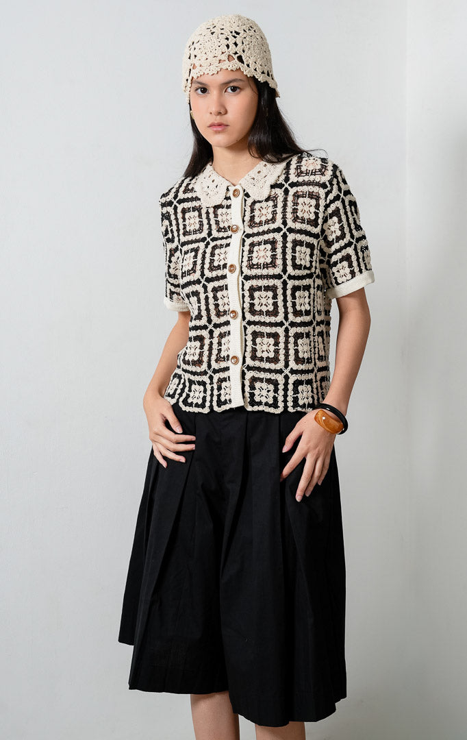 Atasan rajut motif geometris warna hitam (black crochet top) Sorae Top dengan kerah model Peter Pan aksen rajut (crochet-inspired Peter Pan collar), lengan pendek, siluet santai (relaxed silhouette), dan bukaan kancing depan (button-down front). 

