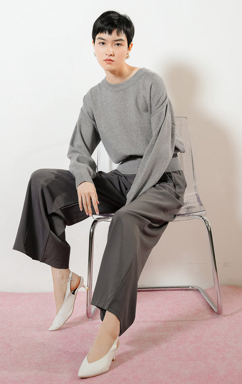 Model wanita mengenakan Cerise Button Hem Knit Sweater warna grey, atasan sweater rajut wanita lengan panjang berwarna abu-abu dengan karet pinggang rib lebar berdetail kancing. 