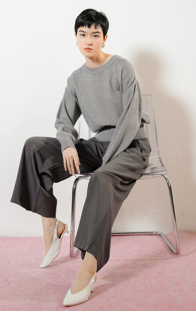 Model wanita mengenakan Cerise Button Hem Knit Sweater warna grey, atasan sweater rajut wanita lengan panjang berwarna abu-abu dengan karet pinggang rib lebar berdetail kancing. 