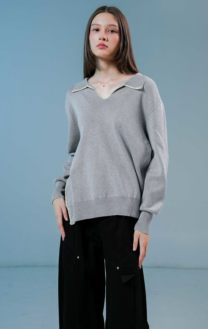 Model wanita mengenakan Maddox V-Neck Contrast Stitch Collared Sweater warna grey, baju sweater rajut wanita lengan panjang berwarna abu-abu dengan detail jahitan kontras putih di kerah.
