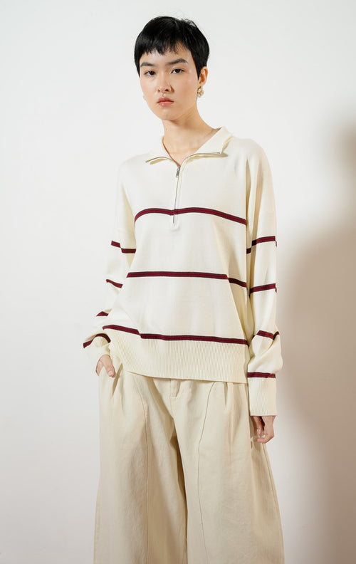Model wanita mengenakan Jayce Half-Zip Striped Pullover Sweater warna ivory, baju atasan sweater rajut wanita lengan panjang warna putih gading motif garis marun dengan kerah ritsleting half-zip. 