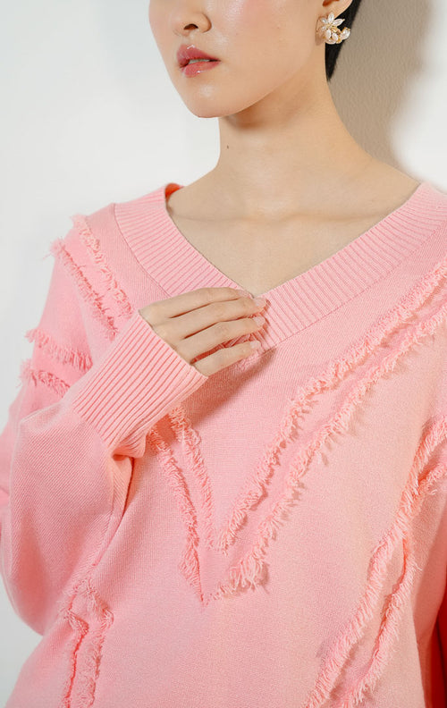 Model wanita mengenakan Wyetta V-Neck Fringe Knit Sweater warna pink, baju sweater rajut wanita leher V warna merah muda pastel dengan detail aksen jumbai rumbai bertekstur modis.