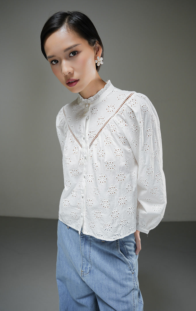 Atasan blouse wanita Sylvia Top warna putih bahan eyelet bordir dengan detail kerah frill rumbai dan kancing depan bungkus yang elegan. 