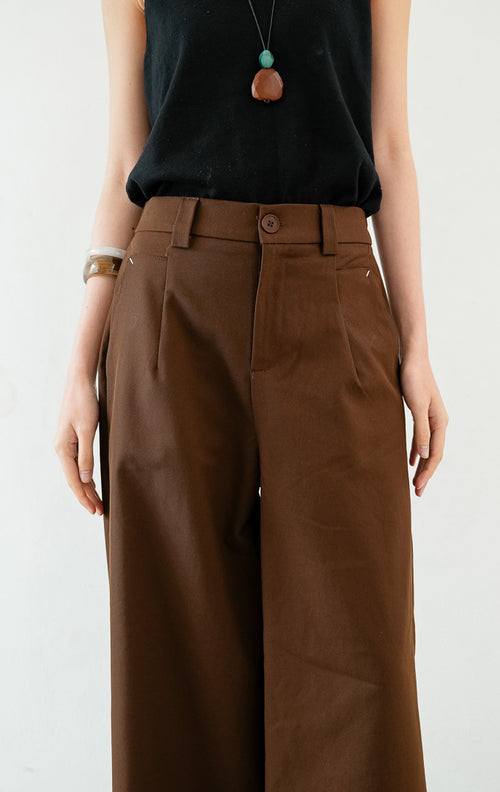 Celana panjang wanita siluet lurus (straight-leg trousers) warna cokelat tua (dark brown) Sylvie Pants dengan ban pinggang terstruktur berloop ikat pinggang (belt loops), kancing depan, saku miring, dan karet elastis di bagian belakang pinggang (elasticated back waistband). 


