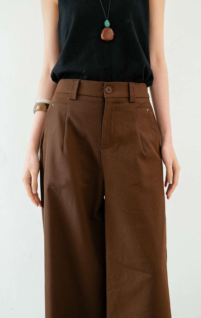 Celana panjang wanita siluet lurus (straight-leg trousers) warna cokelat tua (dark brown) Sylvie Pants dengan ban pinggang terstruktur berloop ikat pinggang (belt loops), kancing depan, saku miring, dan karet elastis di bagian belakang pinggang (elasticated back waistband). 


