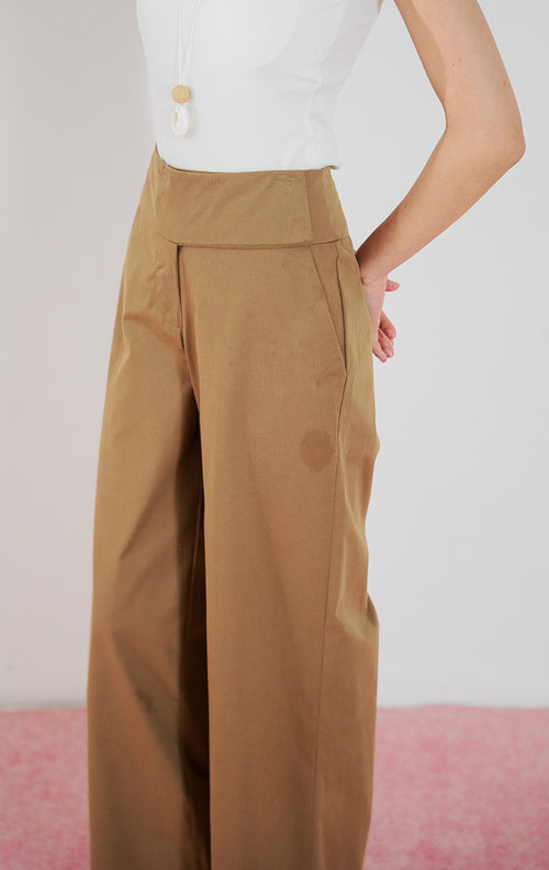 Celana panjang wanita Taffyra Pants warna cokelat (brown) dari This Is April dengan potongan high-waisted dan kaki lebar (wide leg), dipadukan dengan tank top putih.
